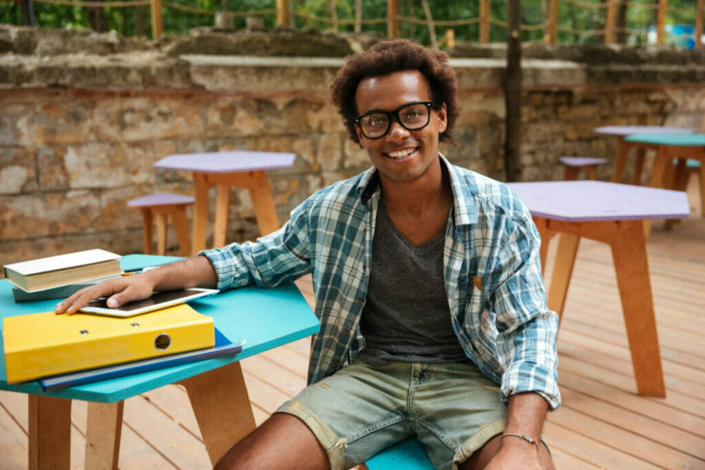 Portrait of cheerful young man in glasses sitting and smiling in outdoor cafe